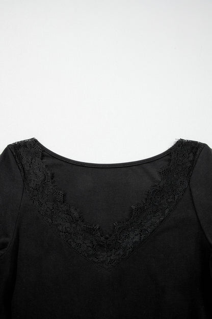Black fitted long sleeve top with floral lace-trim V-neckline and soft stretch fabric styled with white pants.