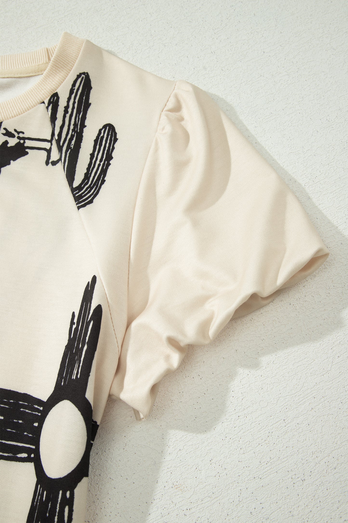Cream Western graphic print top with crew neckline, short sleeves with gathered armholes, and black cowboy boot, cactus, horseshoe, and Southwestern motifs.