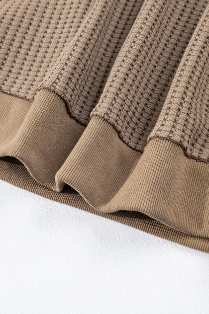 Woman wearing a Mocha textured waffle knit pullover with snap collar, relaxed long sleeves, and ribbed cuffs with white pants.