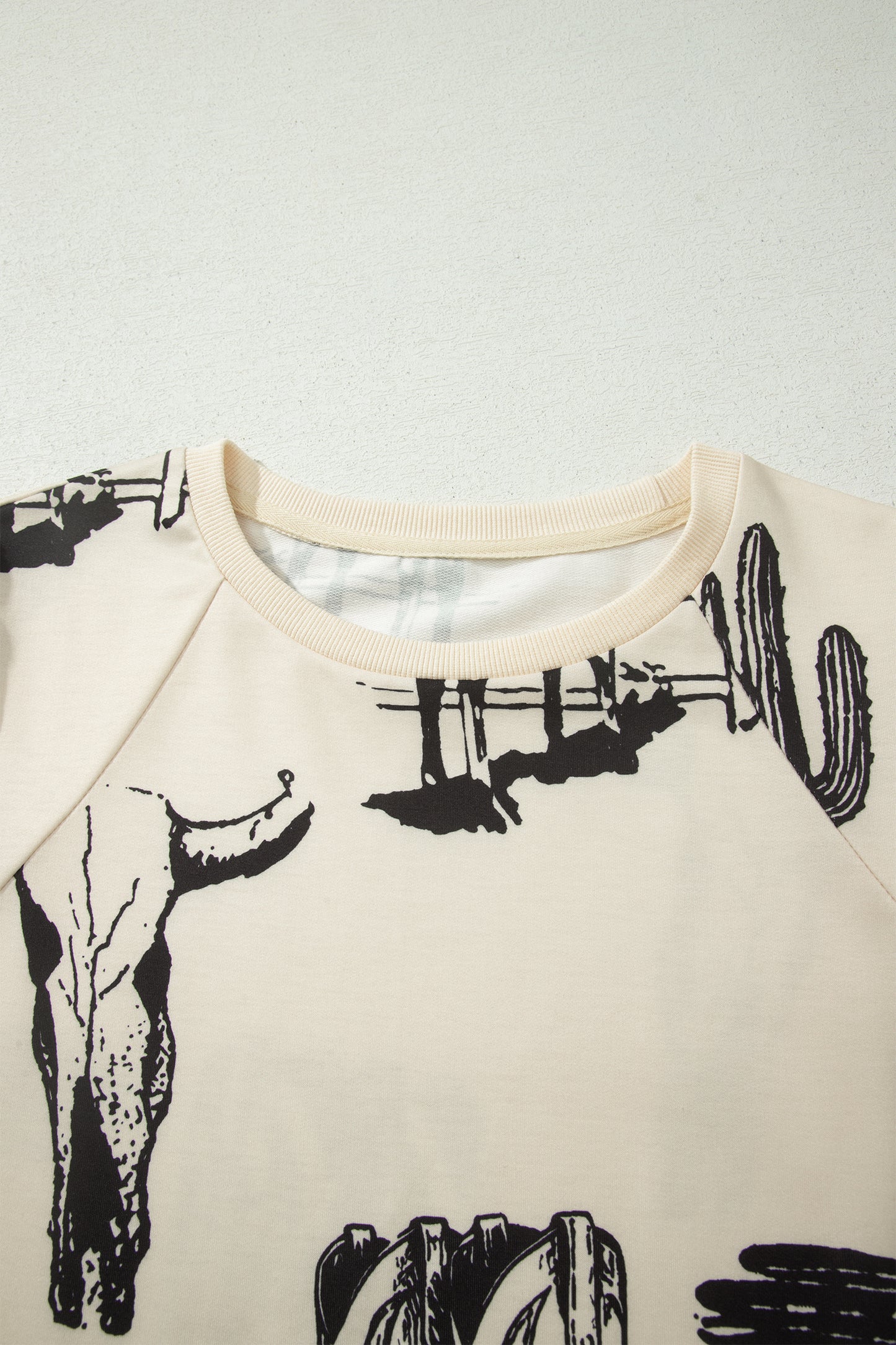 Cream Western graphic print top with crew neckline, short sleeves with gathered armholes, and black cowboy boot, cactus, horseshoe, and Southwestern motifs.
