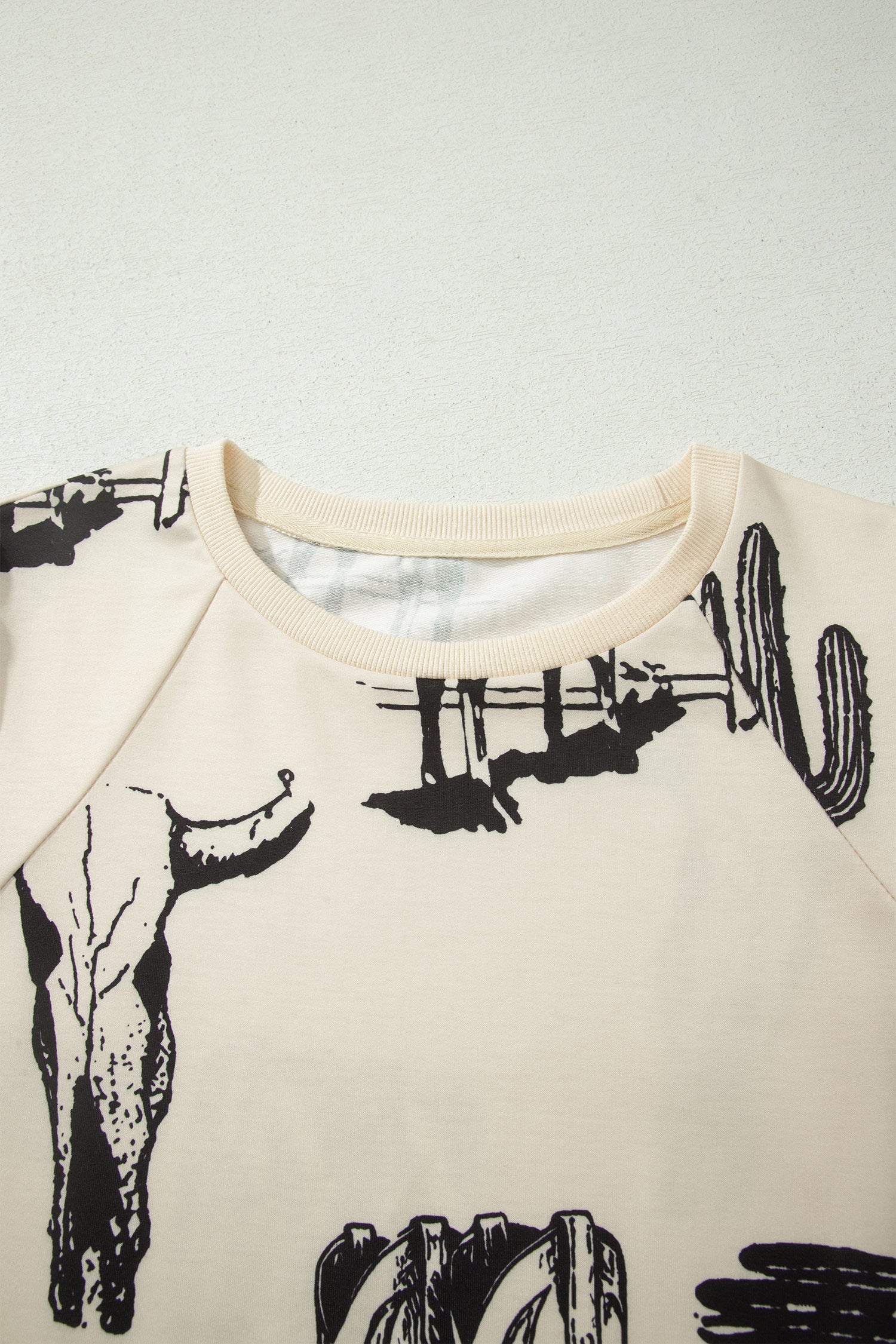 Cream Western graphic print top with crew neckline, short sleeves with gathered armholes, and black cowboy boot, cactus, horseshoe, and Southwestern motifs.