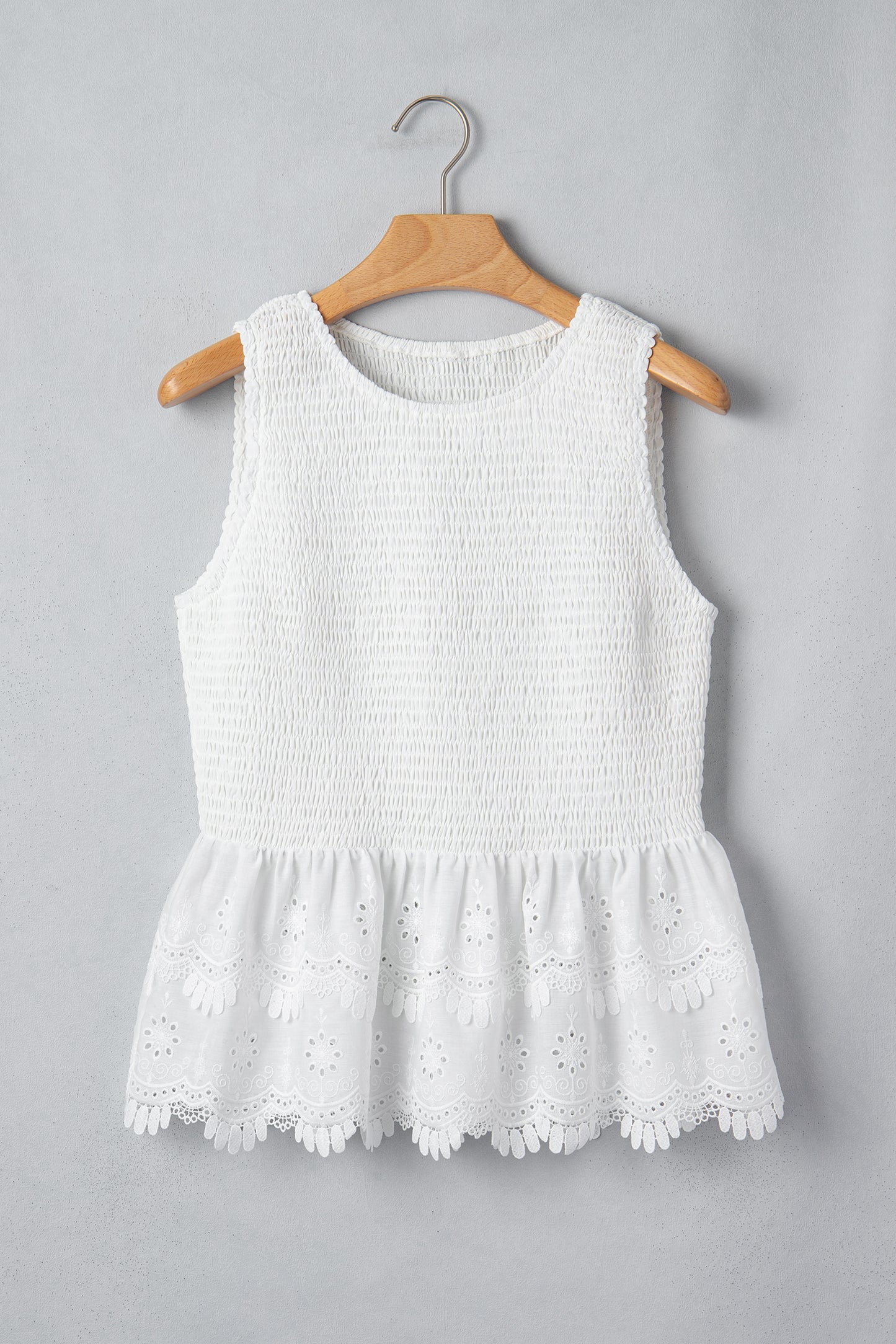 Women's white smocked sleeveless peplum top with embroidered eyelet hem, round neckline, textured bodice, and feminine boutique style.