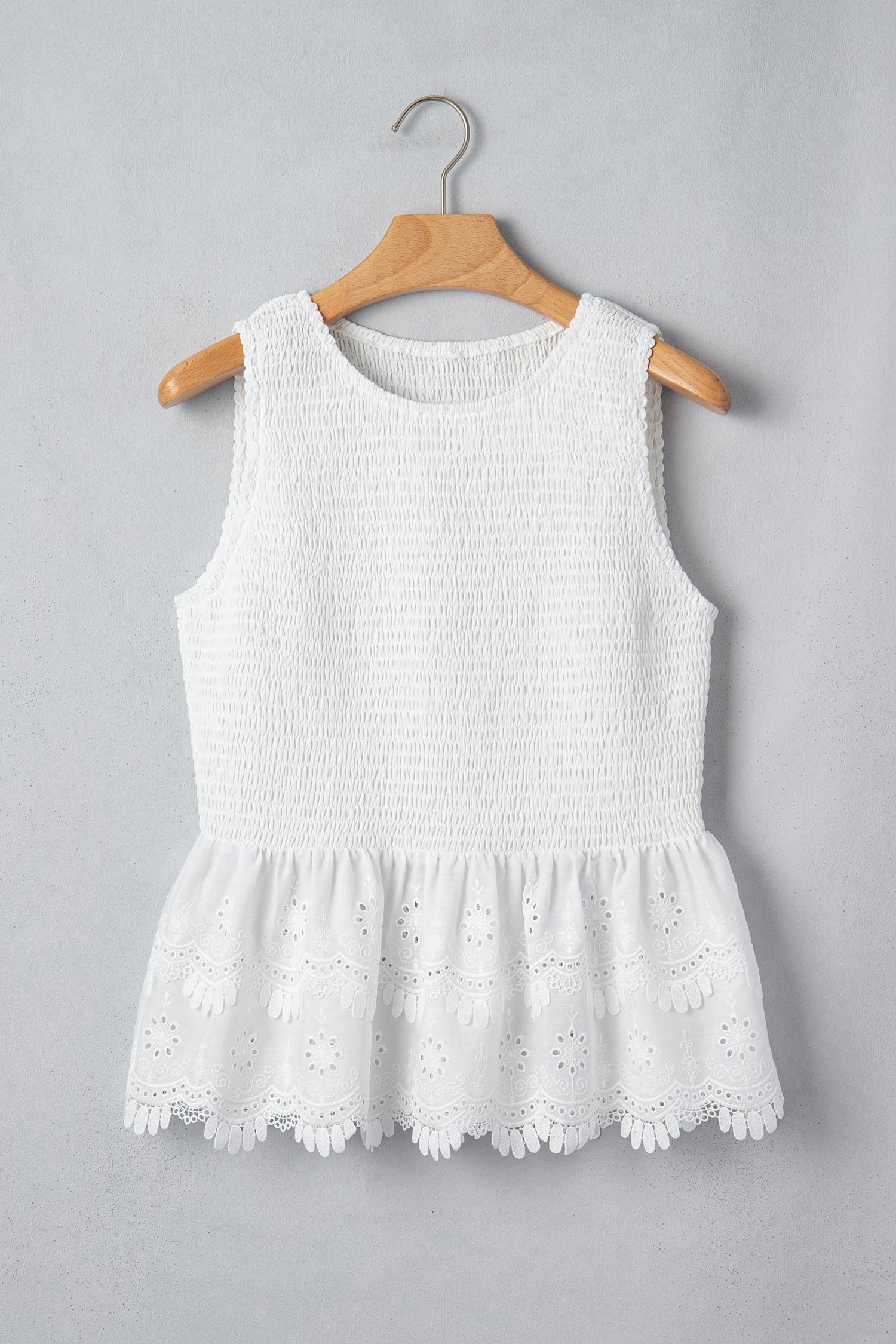 Women's white smocked sleeveless peplum top with embroidered eyelet hem, round neckline, textured bodice, and feminine boutique style.