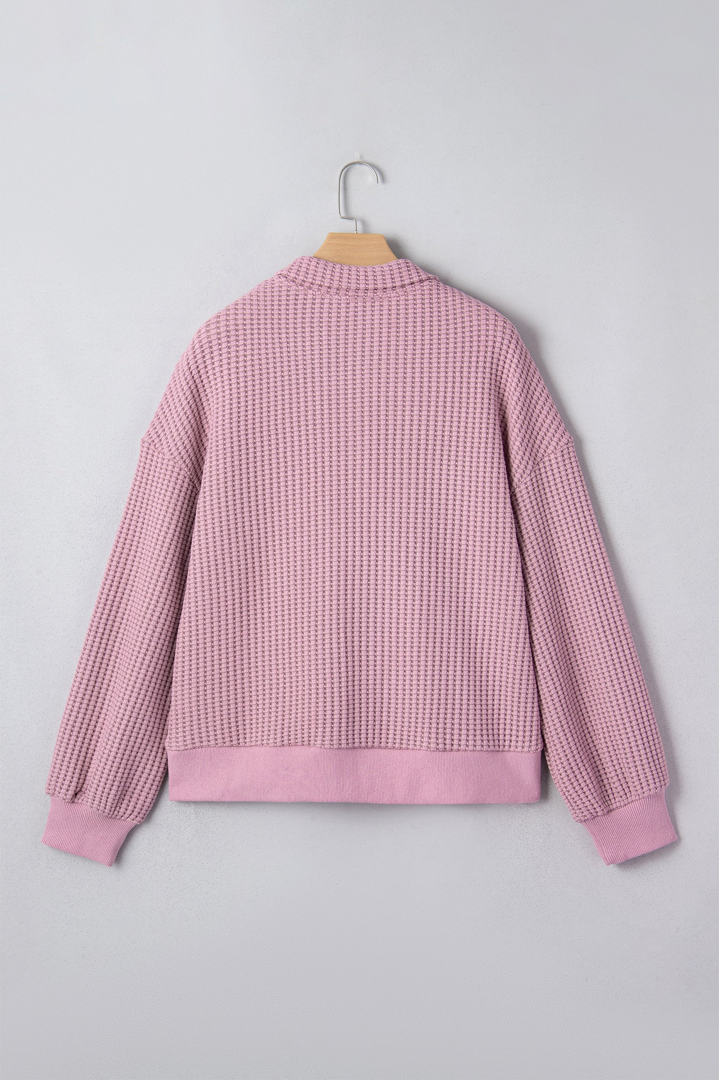 Woman wearing a Blush textured waffle knit pullover with snap collar, relaxed long sleeves, and ribbed cuffs with white pants.