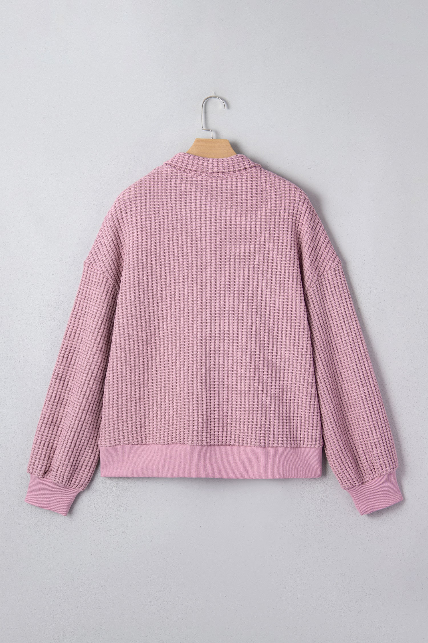 Woman wearing a Blush textured waffle knit pullover with snap collar, relaxed long sleeves, and ribbed cuffs with white pants.
