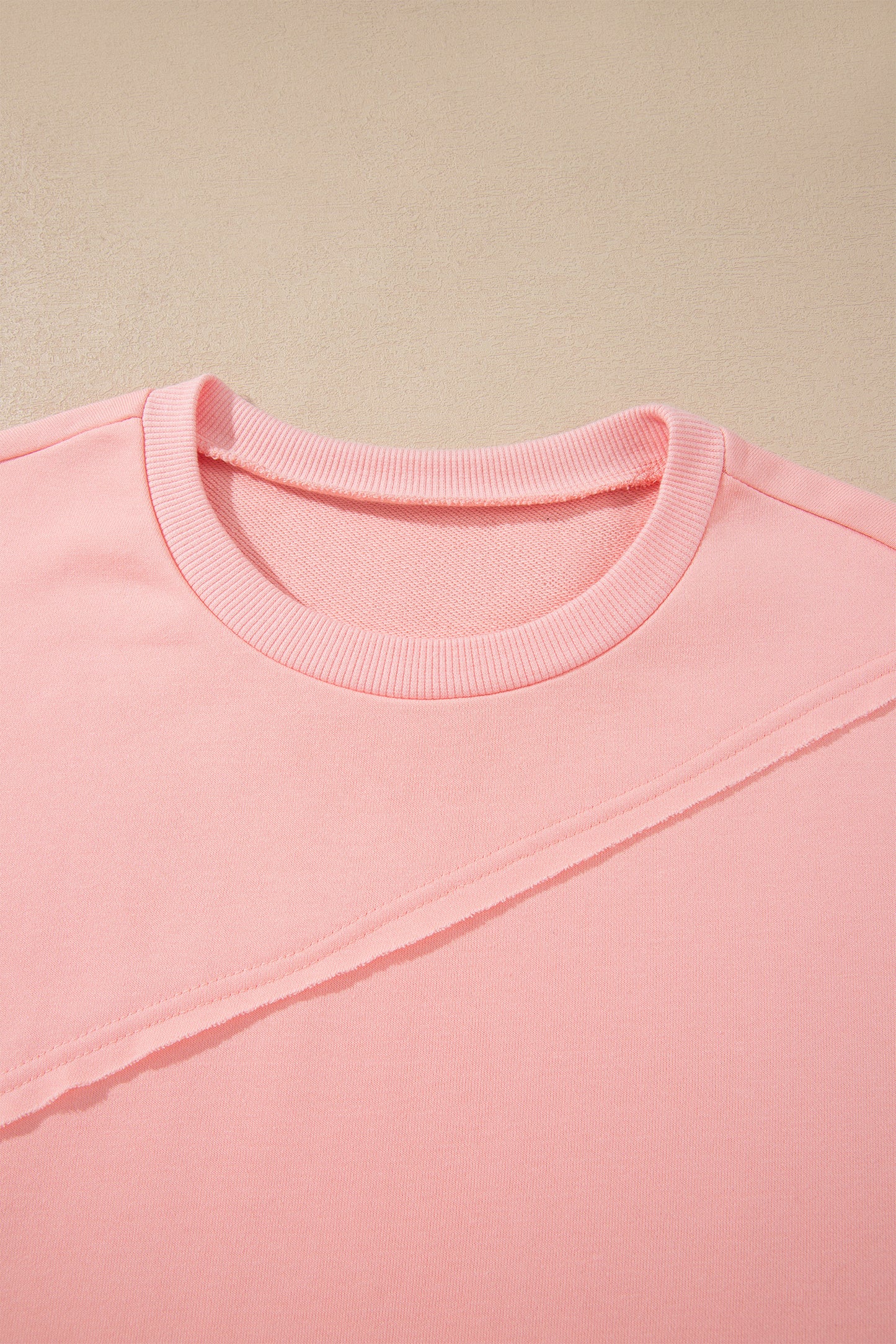 Pink crew neck long sleeve top with asymmetrical paneled body design and blue striped color block sleeves with contrasting orange accents.