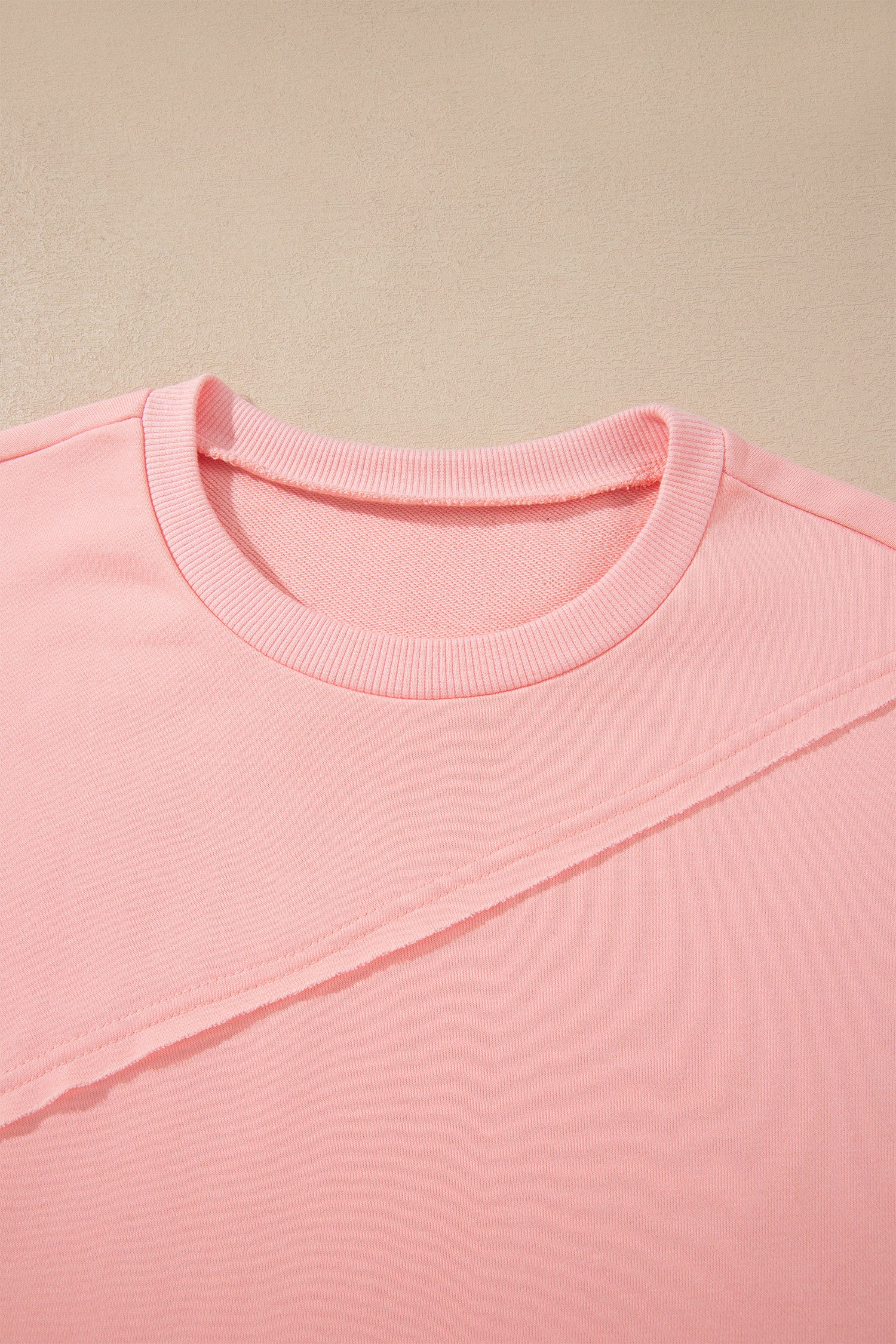 Pink crew neck long sleeve top with asymmetrical paneled body design and blue striped color block sleeves with contrasting orange accents.