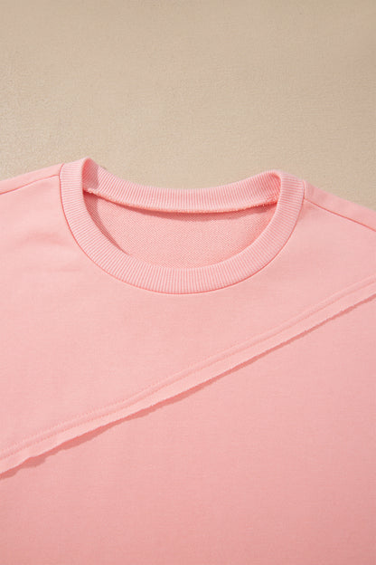 Pink crew neck long sleeve top with asymmetrical paneled body design and blue striped color block sleeves with contrasting orange accents.
