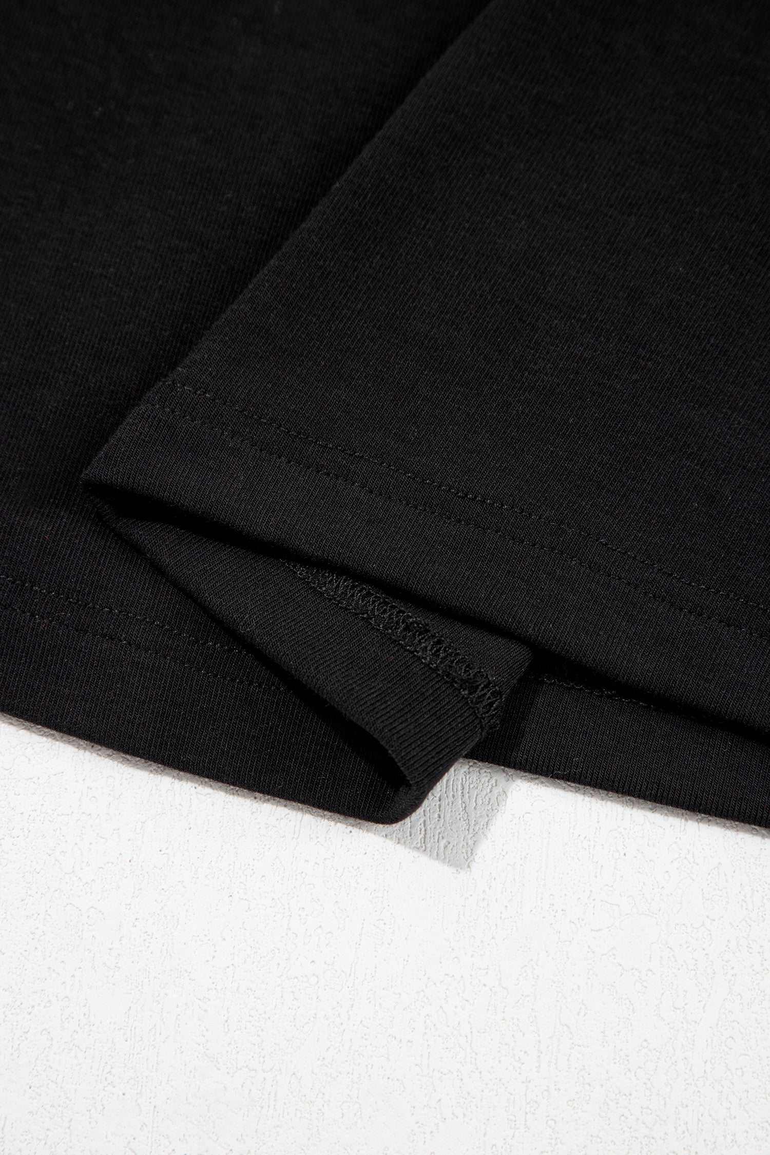 Black fitted long sleeve top with floral lace-trim V-neckline and soft stretch fabric styled with white pants.